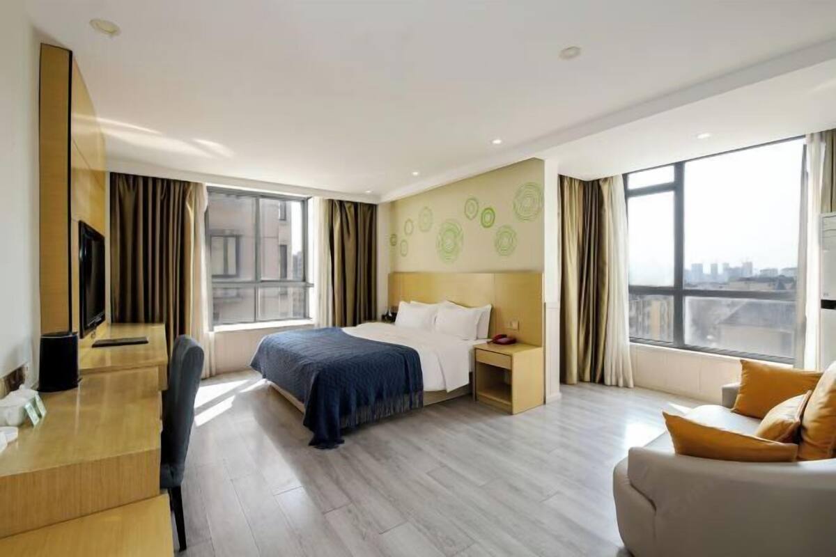 A hotel room with a bed, a desk, a chair, a TV, and large windows.