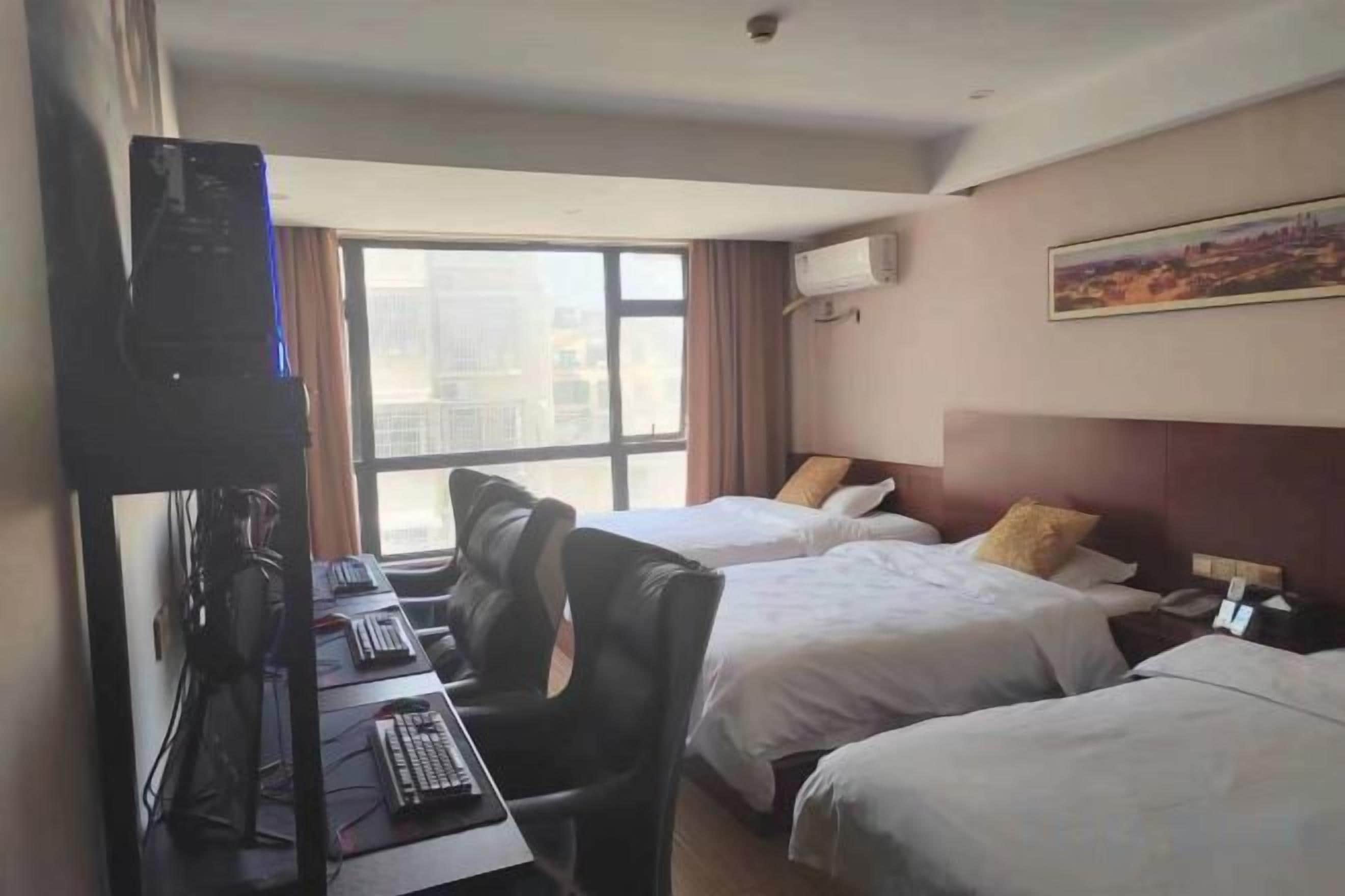 A hotel room with two beds, a desk with a computer, and a window with a city view.