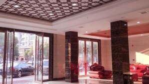 A hotel lobby with a modern design, featuring a patterned ceiling, large glass doors, and red seating. - The Wall Street Holiday Hotel (Yichun)