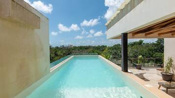 A rectangular swimming pool with clear water, surrounded by a concrete deck and a covered area with seating.