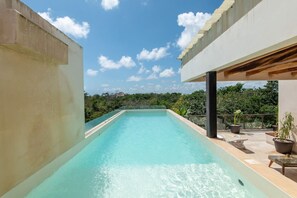 A rectangular swimming pool with clear water, surrounded by a concrete deck and a covered area with seating. - Jungle Loft Suite - Santuario Hotel Boutique (Tulum)