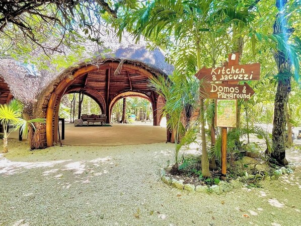 A rustic wooden structure with a thatched roof, surrounded by lush greenery.