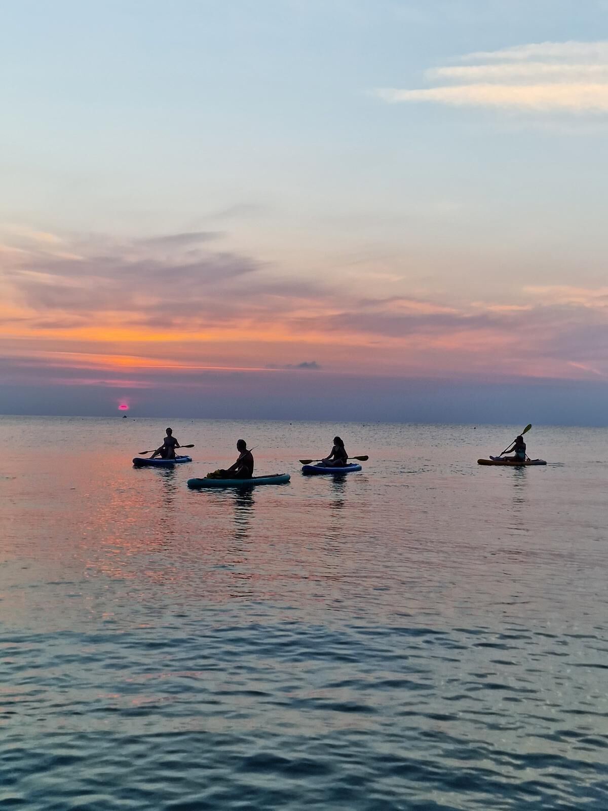 A calm body of water with kayakers in the distance during sunset.