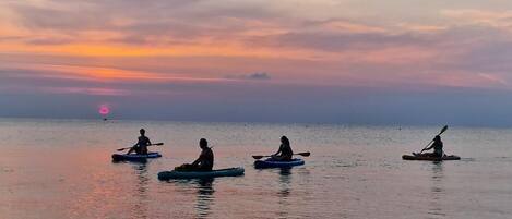 A calm body of water with kayakers in the distance during sunset.