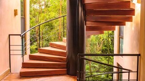 Un escalier en colimaçon avec des marches en bois et des rampes en métal, menant à une pièce offrant une vue sur une végétation luxuriante.