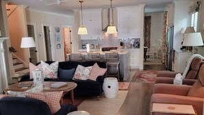 Een moderne woonkamer met een donkere bank, een ronde salontafel en een eethoek met een witte tafel en stoelen.
