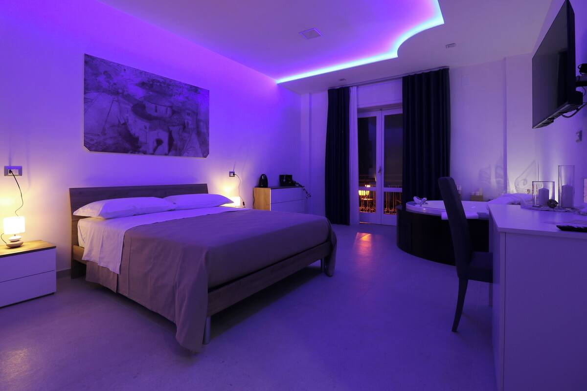 Une chambre d’hôtel moderne équipée d’un lit, de tables de chevet, d’un bureau et d’une grande fenêtre.