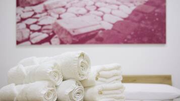 A stack of white towels on a wooden surface with a white pillow and a pink and white photograph on the wall.