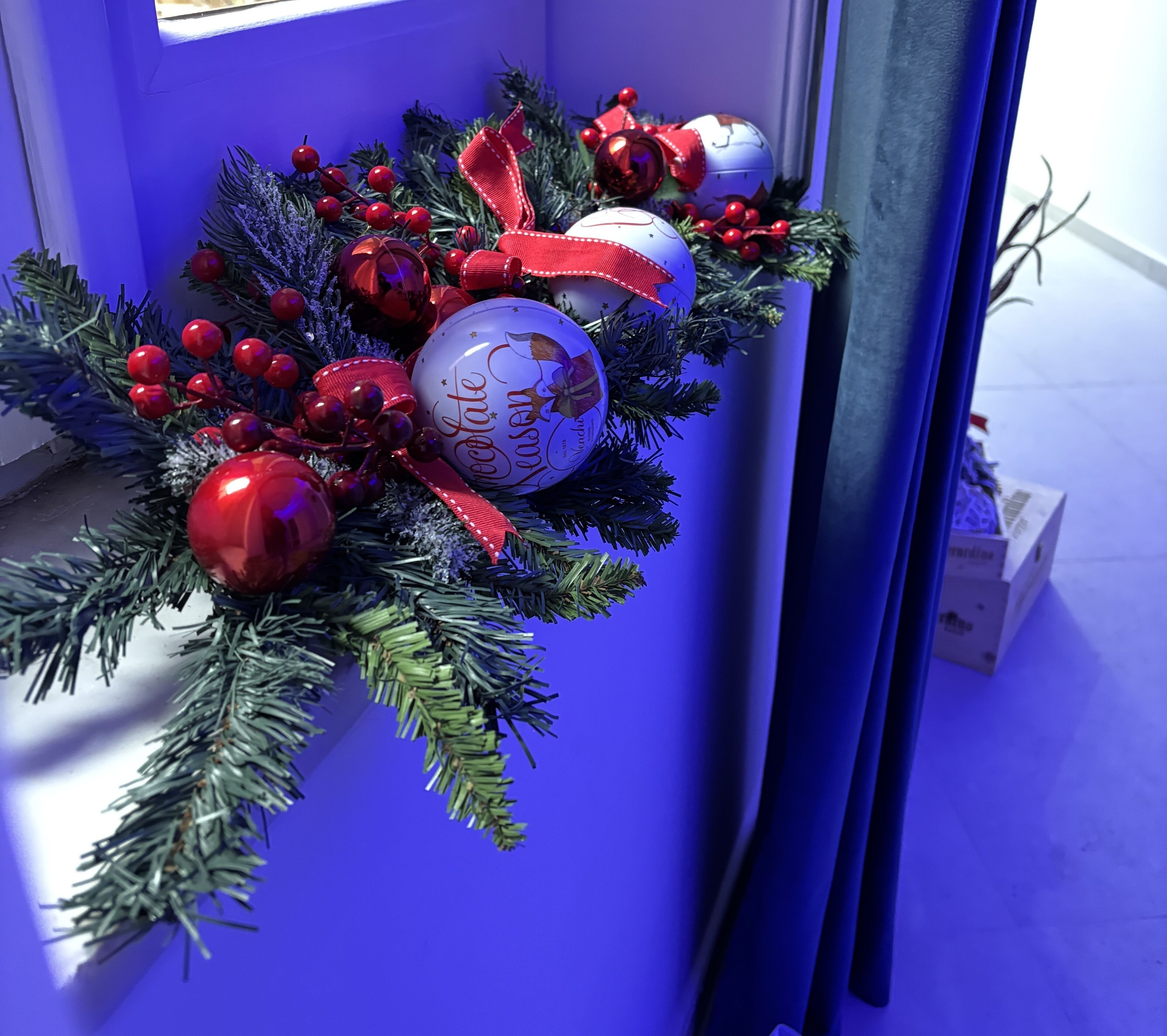 A Christmas wreath with red and white ornaments, including a 'Keenan's' chocolate ornament, hanging on a door.