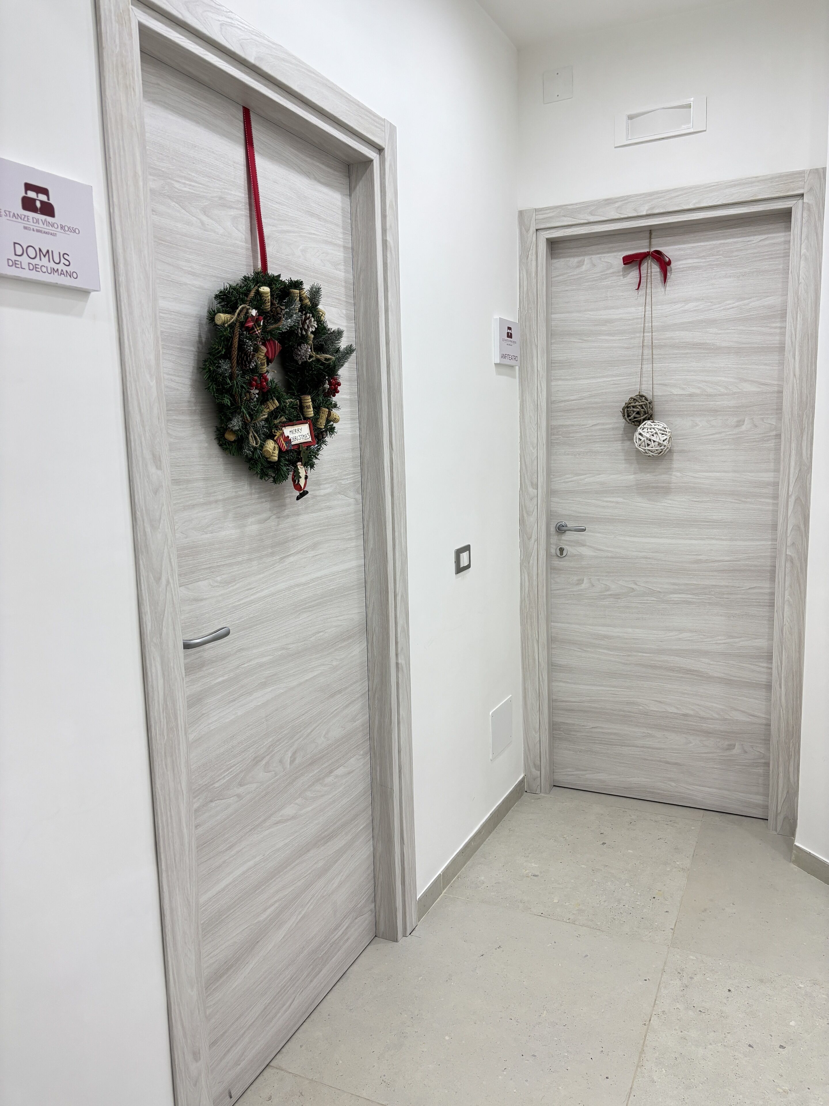 A hallway with two doors, one with a Christmas wreath and the other with a decorative ball.