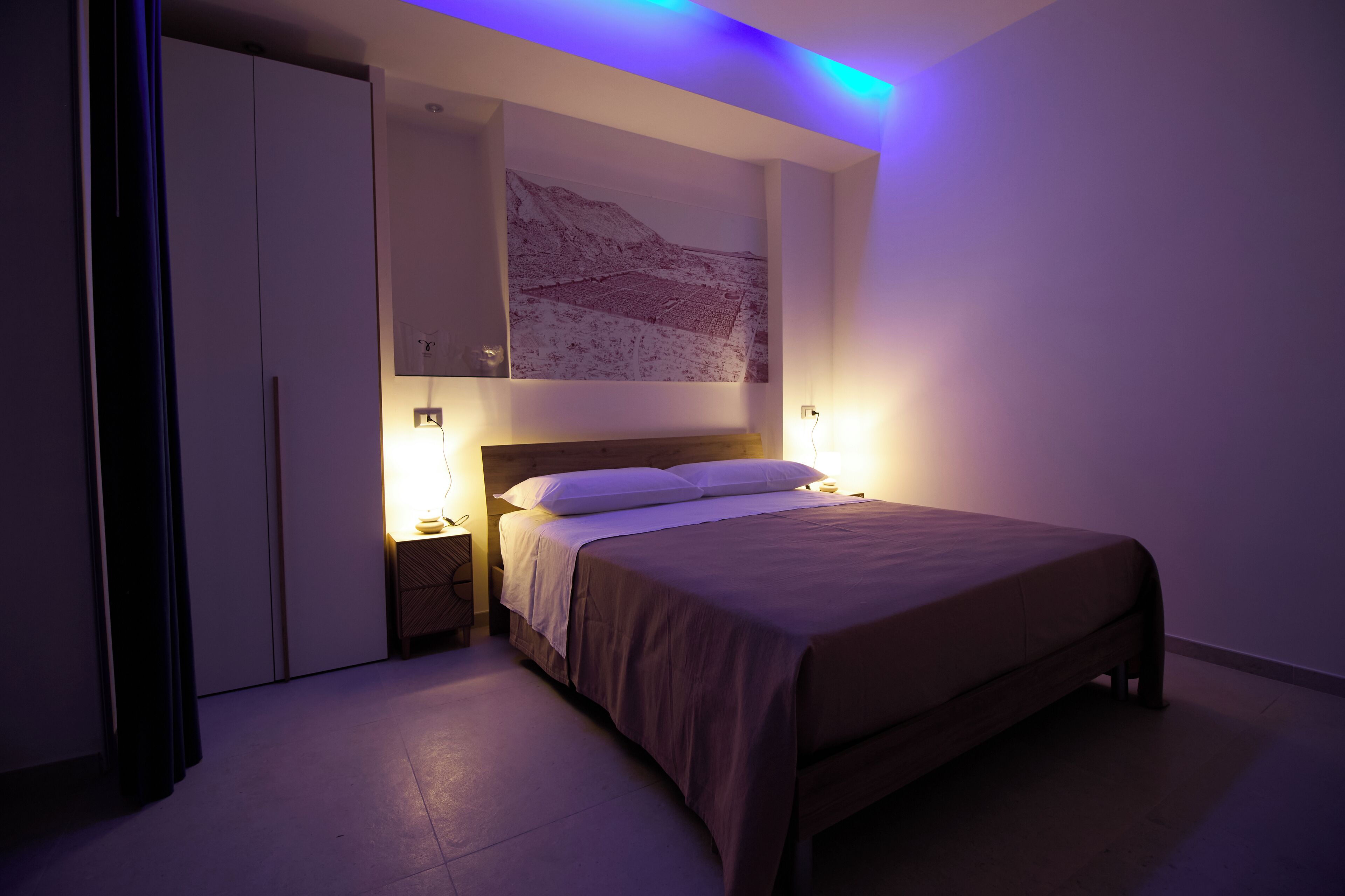Un dormitorio con una cama, mesitas de noche, una obra de arte en la pared y un armario.