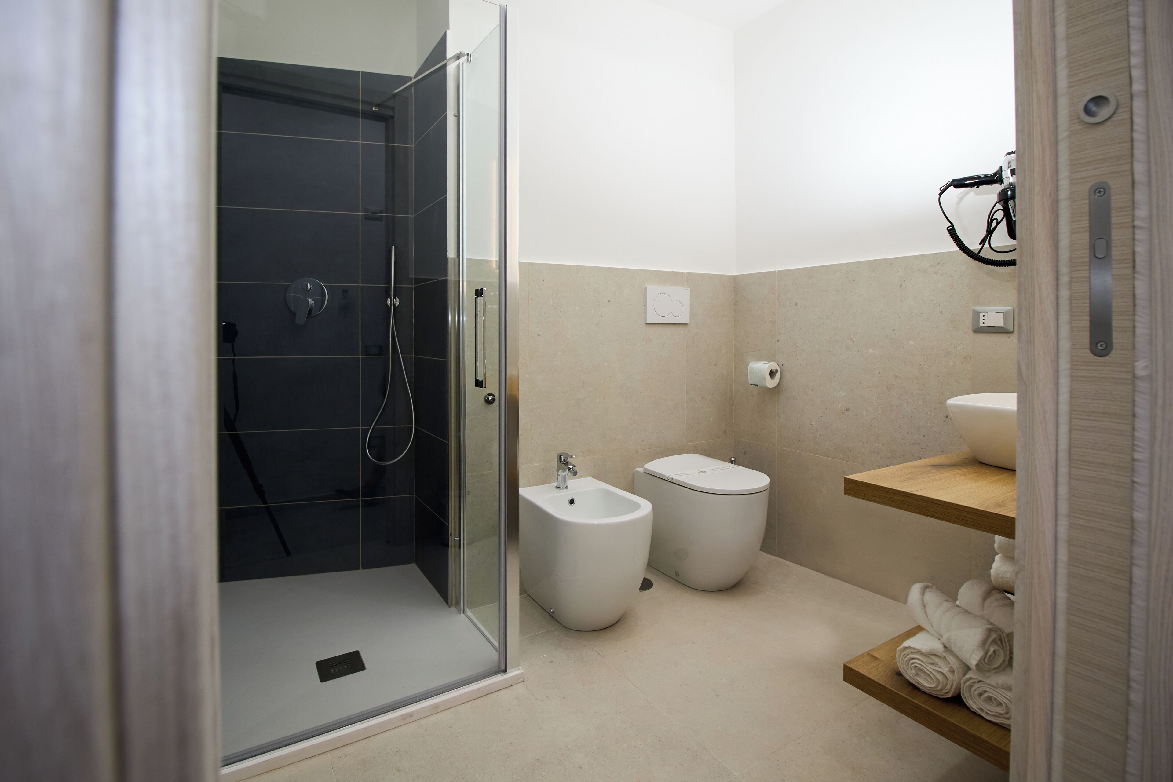 A modern bathroom with a glass shower enclosure, two bidets, a sink, and a towel rack.