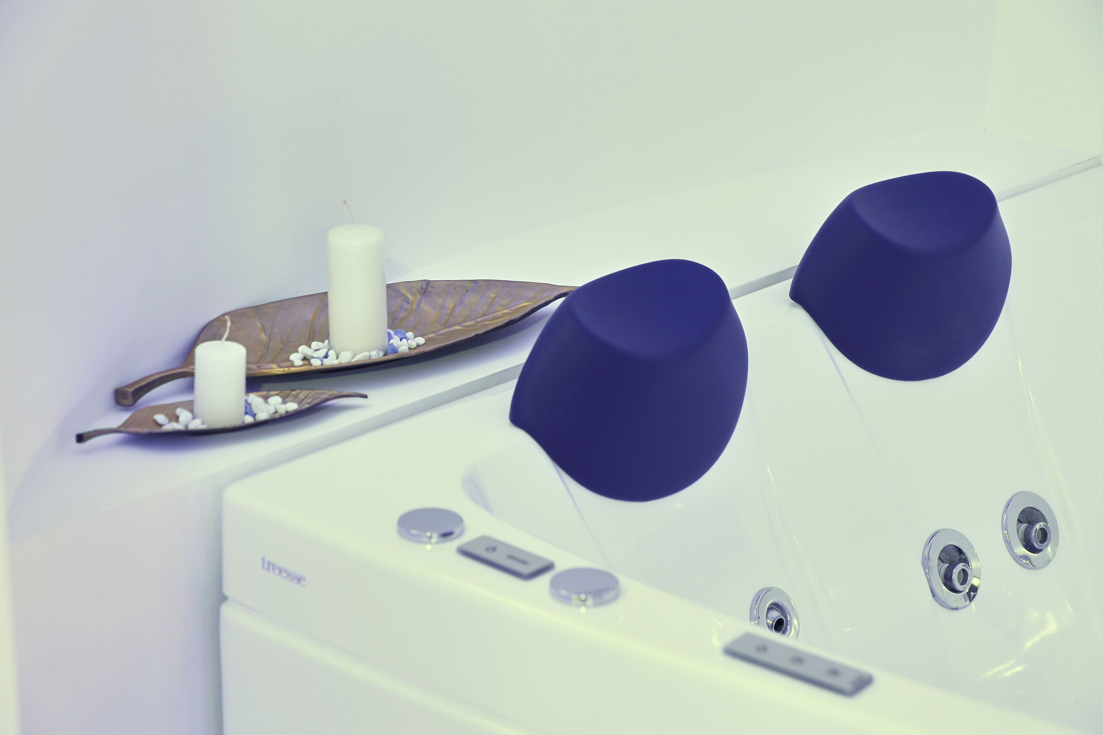 Une baignoire blanche avec deux robinets bleus, une bougie blanche et une feuille décorative ornée de fleurs blanches.