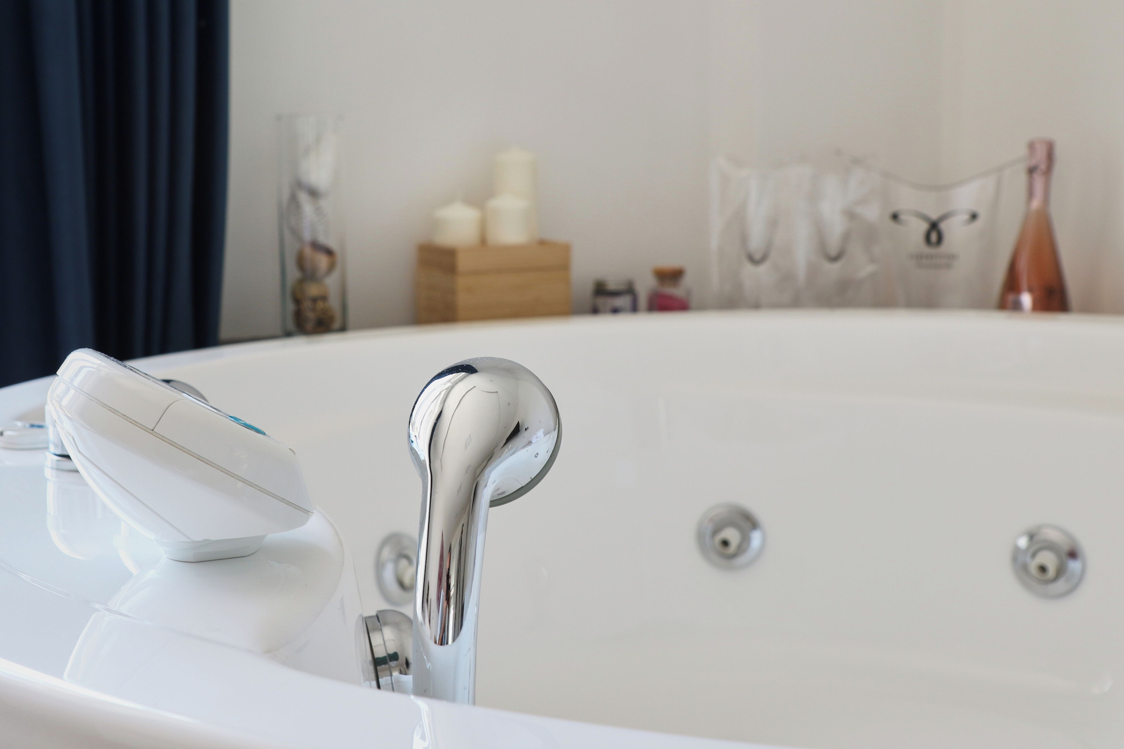 A modern bathroom with a white bathtub, a handheld showerhead, and a bottle of champagne.