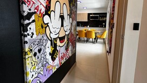 A hallway with a vibrant graffiti mural on the left wall, leading to a modern kitchen area with yellow chairs and a dining table. - Luxury Condo at Viva Jaco Residence (Jaco)