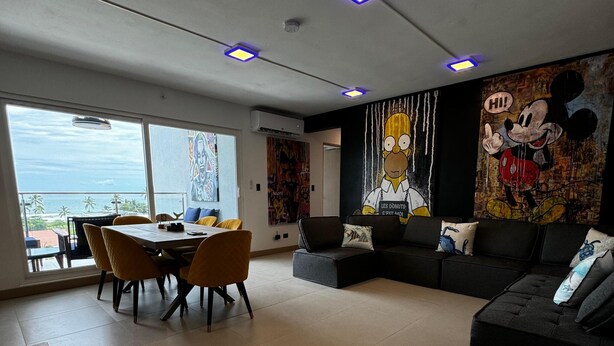 A modern living room with a dining area, large windows, and a mural of Mickey Mouse. - Luxury Condo at Viva Jaco Residence (Jaco)
