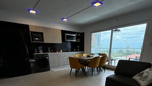 A modern living room with a black sofa, a dining table with yellow chairs, and a kitchen area with a microwave and oven. - Luxury Condo at Viva Jaco Residence (Jaco)