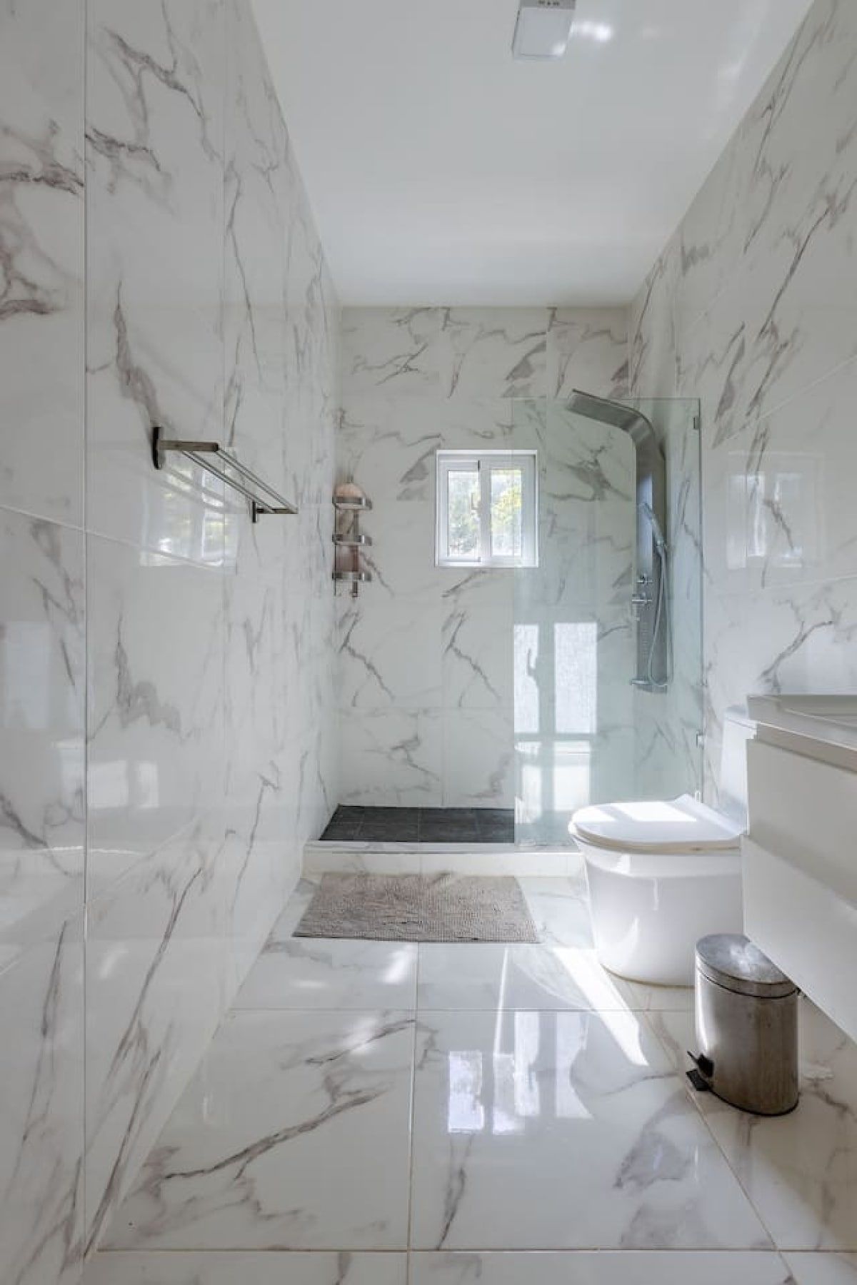 A bathroom with marble walls, a glass shower enclosure, a toilet, and a sink.