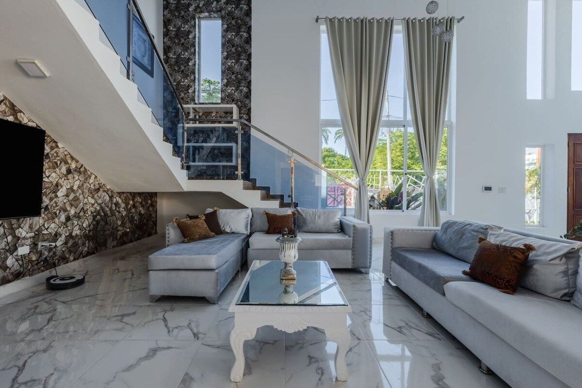 Un salon moderne avec une table basse en verre, deux canapés, un escalier et un mur en pierre.