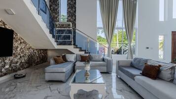 Un salon moderne avec une table basse en verre, deux canapés, un escalier et un mur en pierre.
