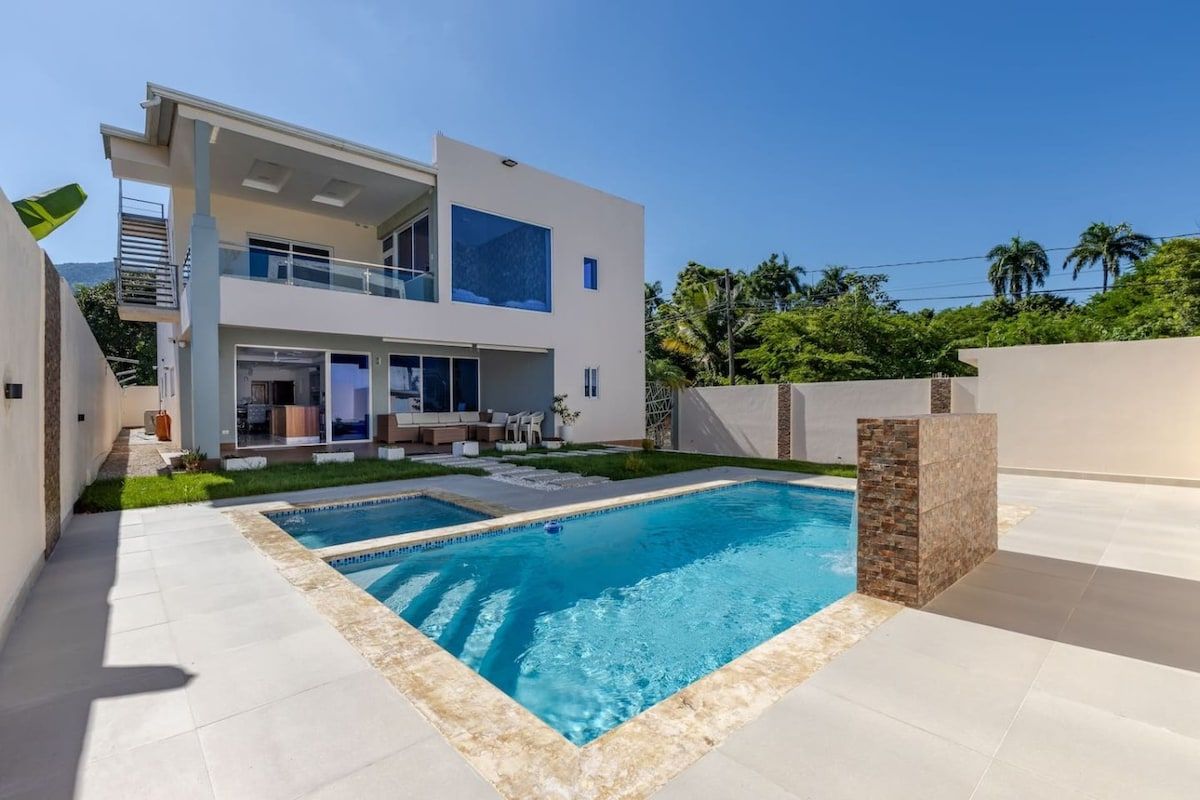 Une maison moderne à deux étages, dotée d’une piscine, d’un espace extérieur aménagé et offrant une vue sur un ciel dégagé.