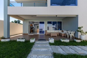Een modern, twee verdiepingen hoog huis met een overdekt terras, buitenmeubels en een pad naar de ingang.