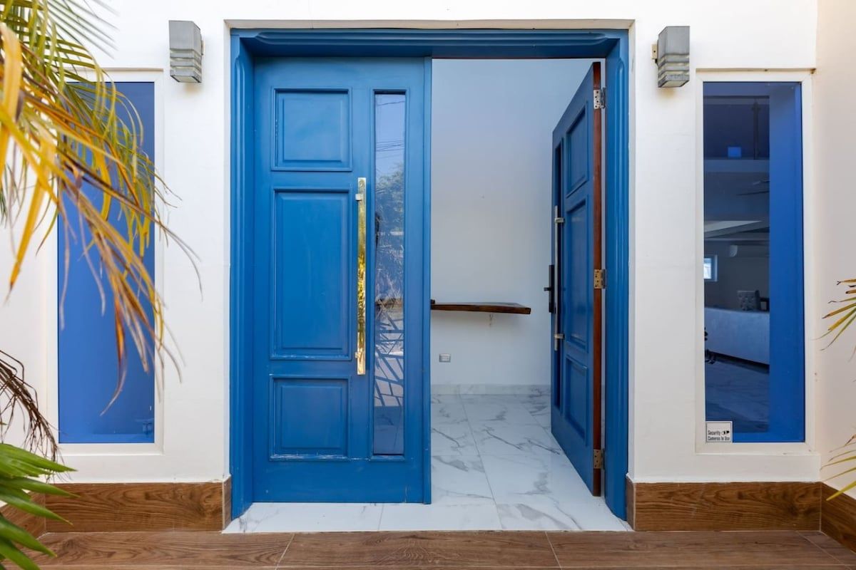 A blue door with a security panel, a wooden floor, and a white wall with a small window.