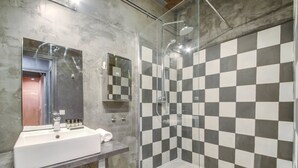A bathroom with a checkered tile wall, a glass shower enclosure, a white sink, and a mirror. - Paris Marais Lombards (Paris)