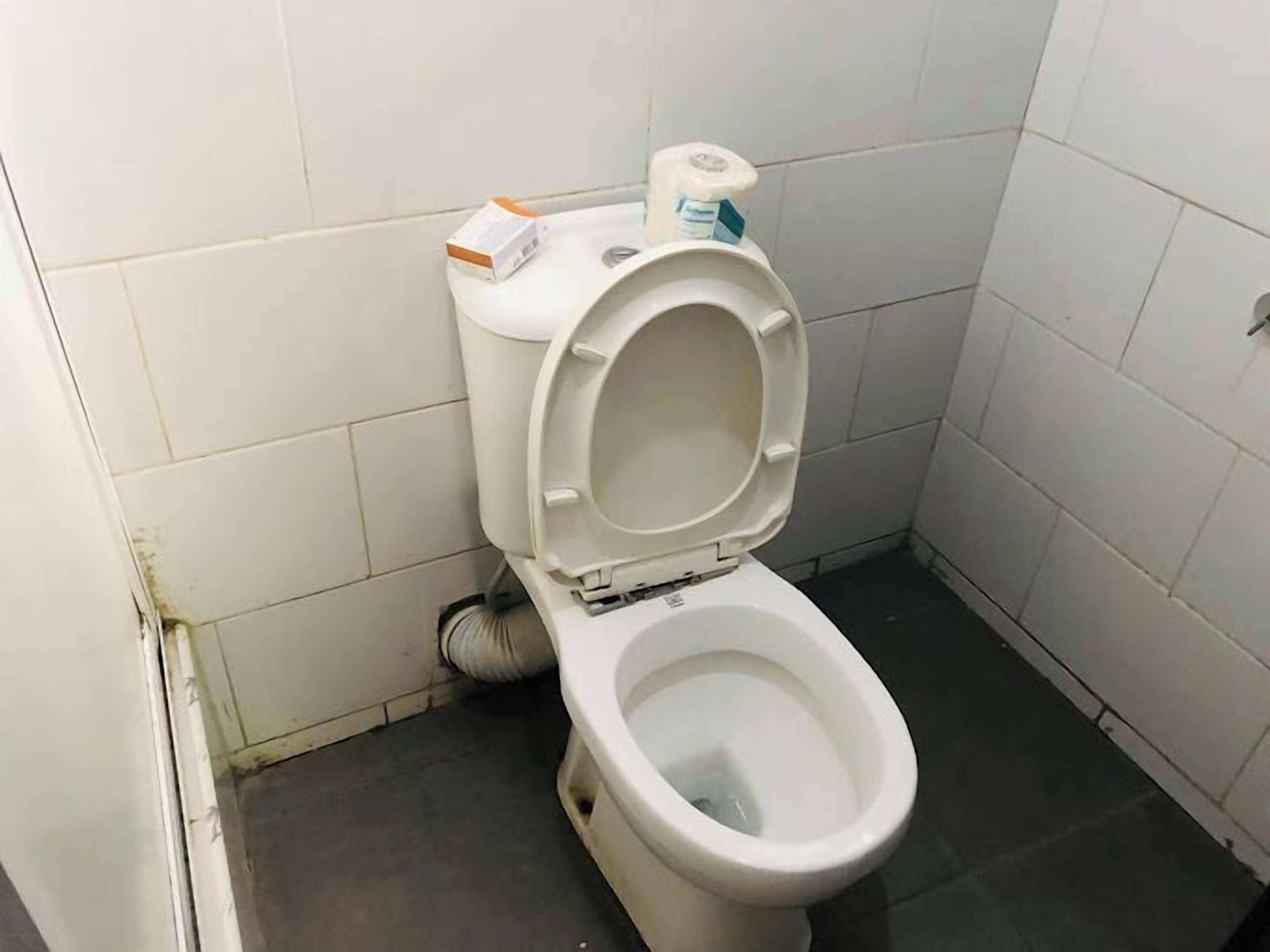 Een standaard wit toilet in een kleine betegelde badkamer met een zwarte vloer.