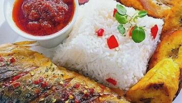 Un plato con arroz blanco, un pescado entero, plátanos fritos y un tazón de salsa roja.