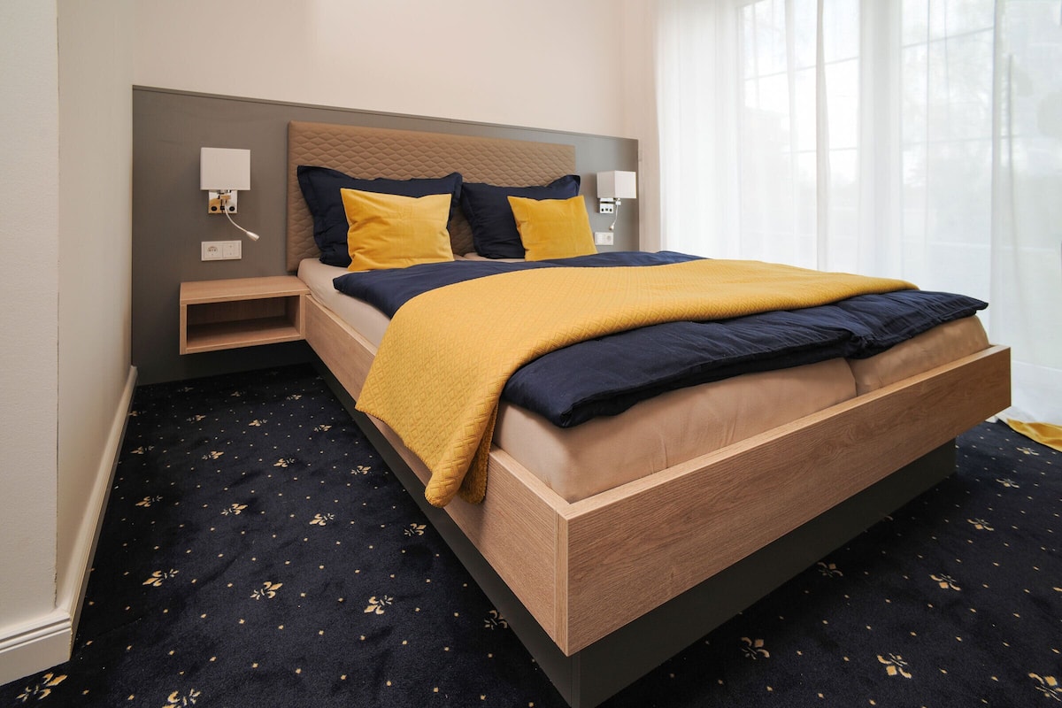 A modern hotel room with a wooden bed, a nightstand, and a bedside table.