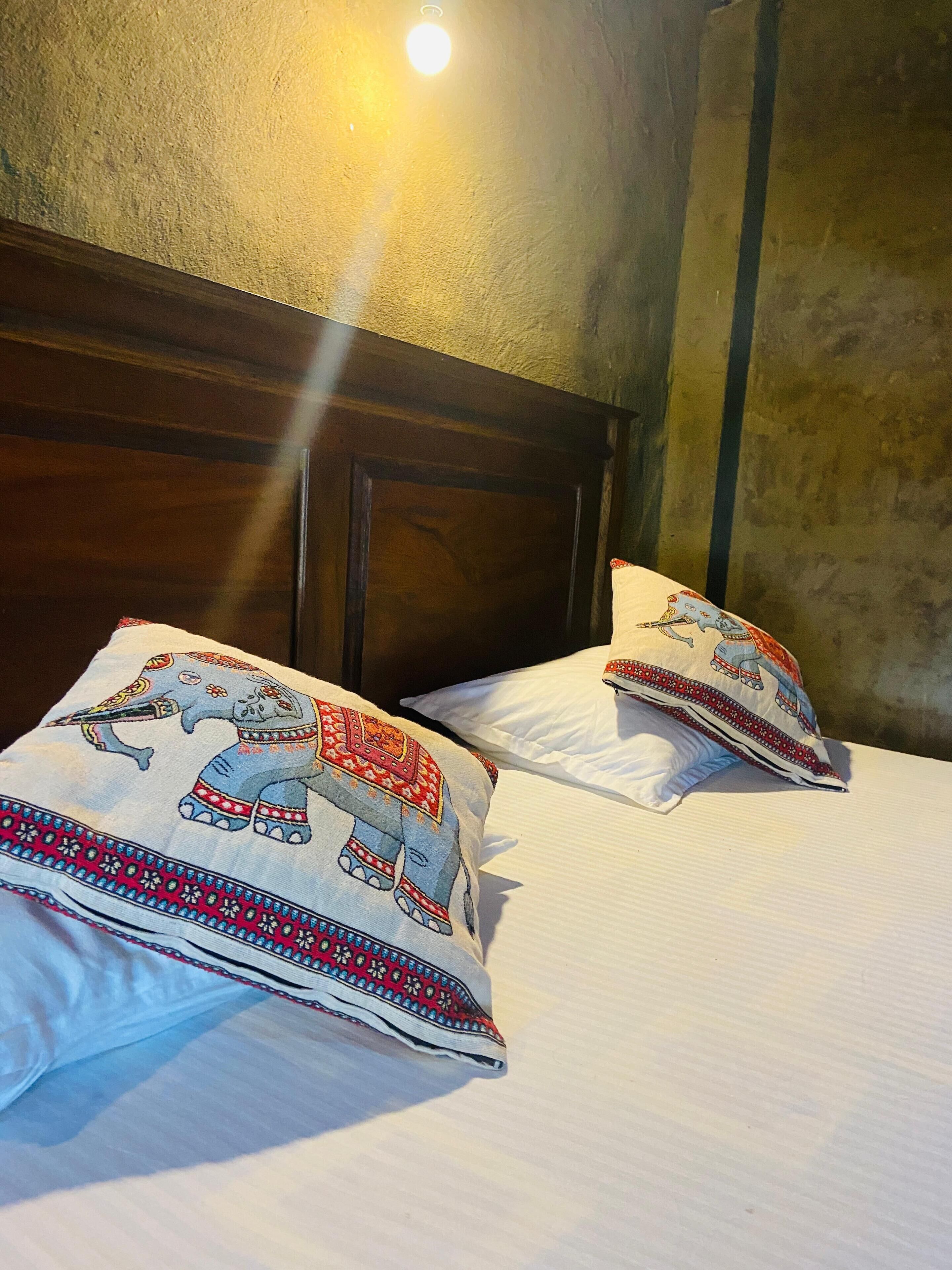 Una cama con dos almohadas decoradas con diseños de elefantes, un cabecero de madera y una pared con textura.