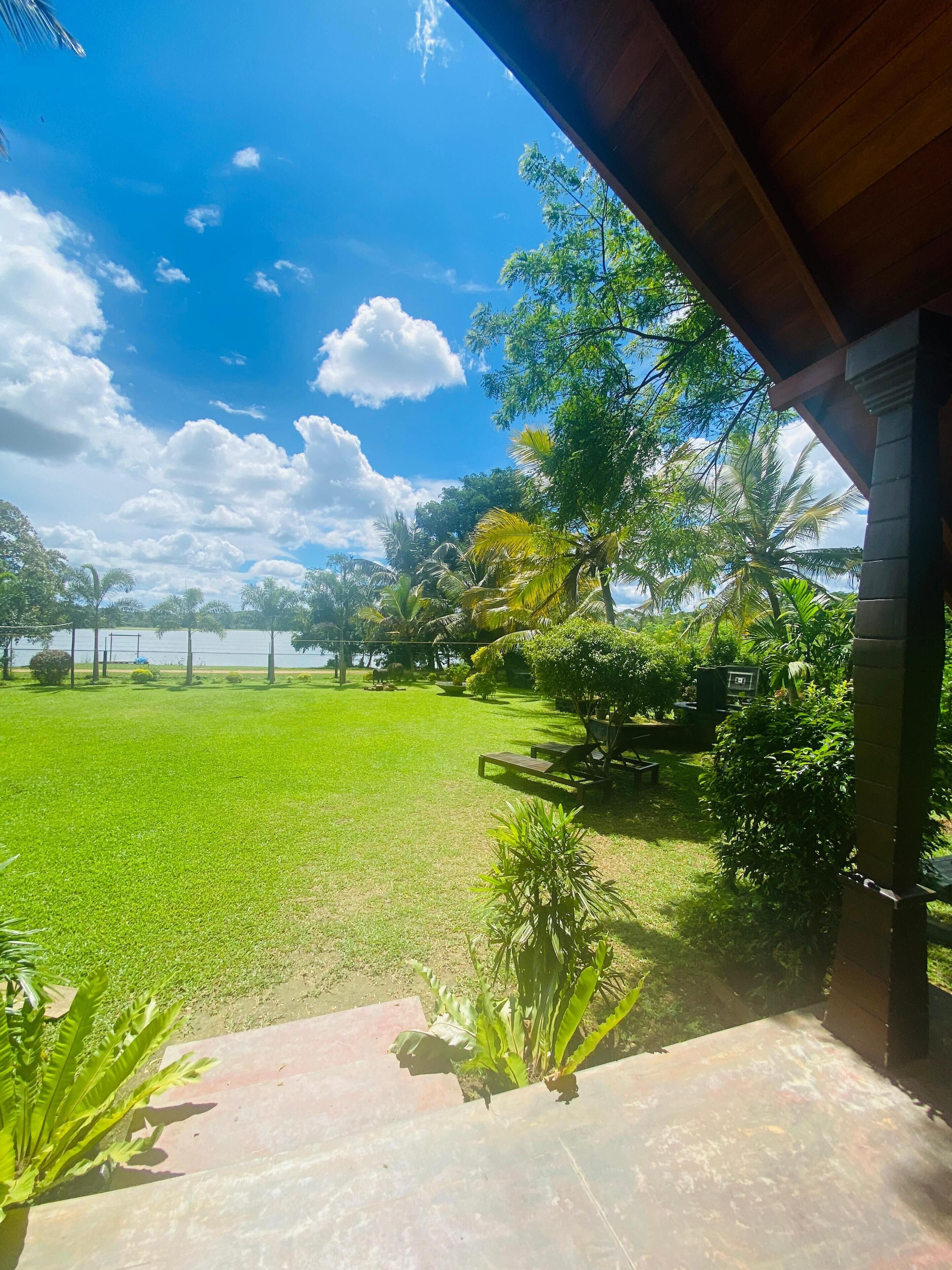 A view from a covered porch overlooking a lush green lawn and a body of water.