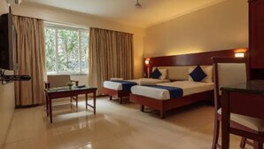 A hotel room with two single beds, a small table, a chair, a TV, and a window with curtains. - Magnus Riverside Boutique Hotels (Pune)