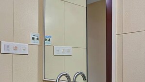A bathroom with a large mirror, two wall-mounted light switches, and a metallic faucet. - Magnus Riverside Boutique Hotels (Pune)
