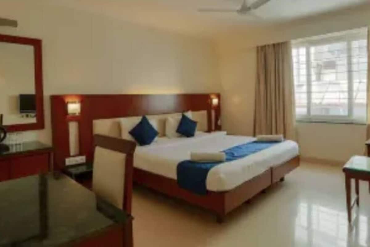 A hotel room with a large bed, a desk, a chair, a TV, and a window with curtains.