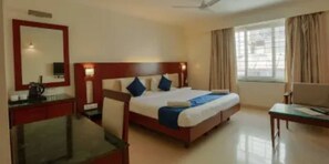 Habitación de hotel con una cama grande, un escritorio, una silla, un televisor y una ventana con cortinas.