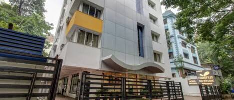 A modern hotel with a curved facade, multiple balconies, and a gated entrance.