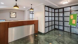 A reception area with a wooden counter, pendant lighting, a large window with a view, and a green easel with papers. - Magnus Riverside Boutique Hotels (Pune)