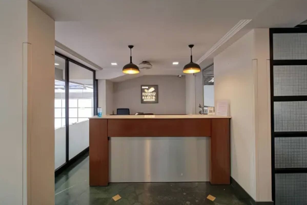 A reception desk with a wooden counter and a glass partition, two pendant lights, and a wall-mounted sign.