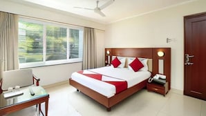 Habitación de hotel con cama, escritorio, silla, ventana con cortinas, ventilador de techo y puerta.