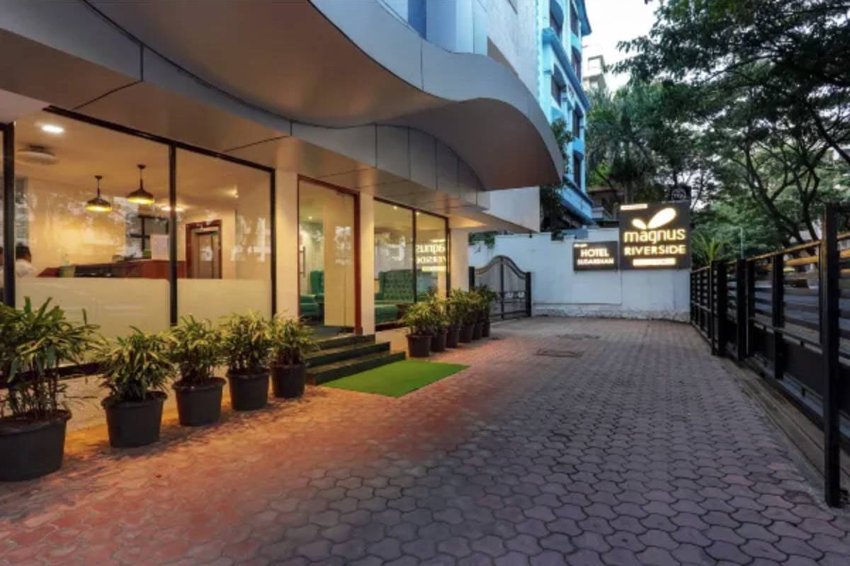 A hotel entrance with a modern design, glass doors, and a sign for 'Magnus Riverside Hotel'.