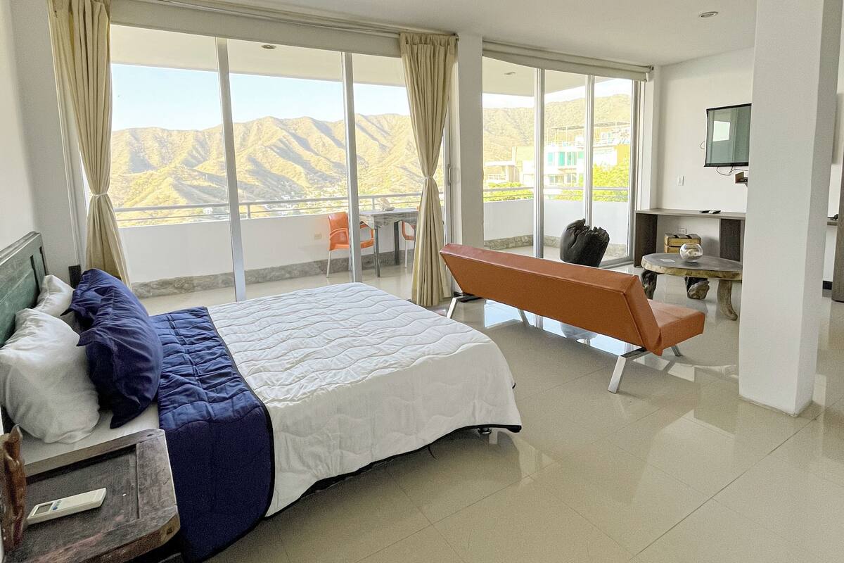 A modern hotel room with a large bed, a bench, a desk, and a TV.
