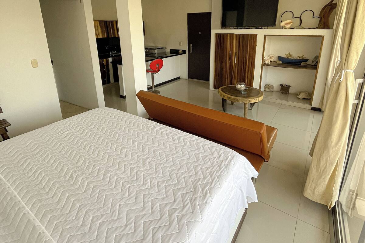 A hotel room with a large bed, a small seating area, a kitchen, and a TV.