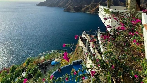 A coastal view with a stone building overlooking a clear blue sea and distant mountains. - HOTEL TNT MIRADOR (Santa Marta)
