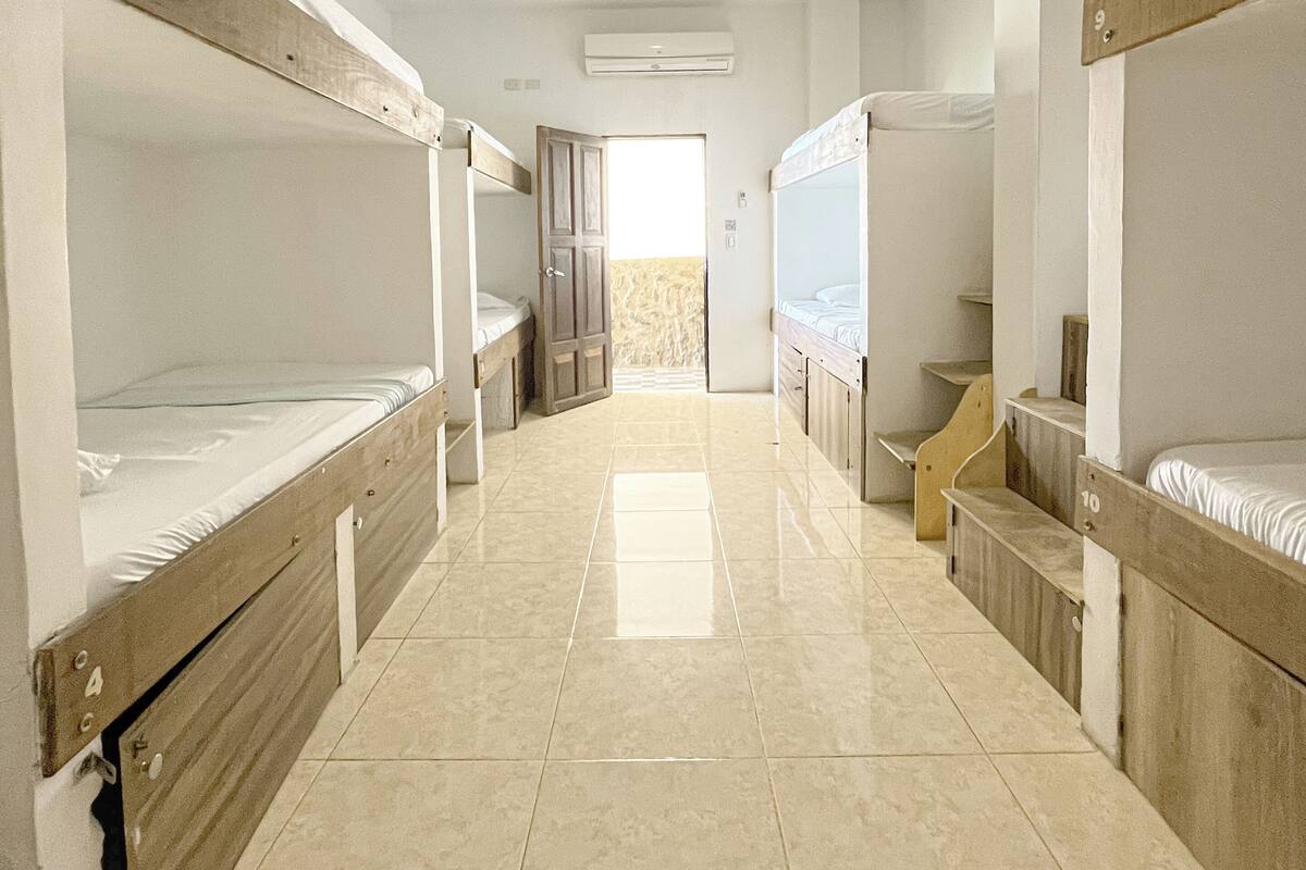 A dormitory room with bunk beds, a tiled floor, and an air conditioning unit.
