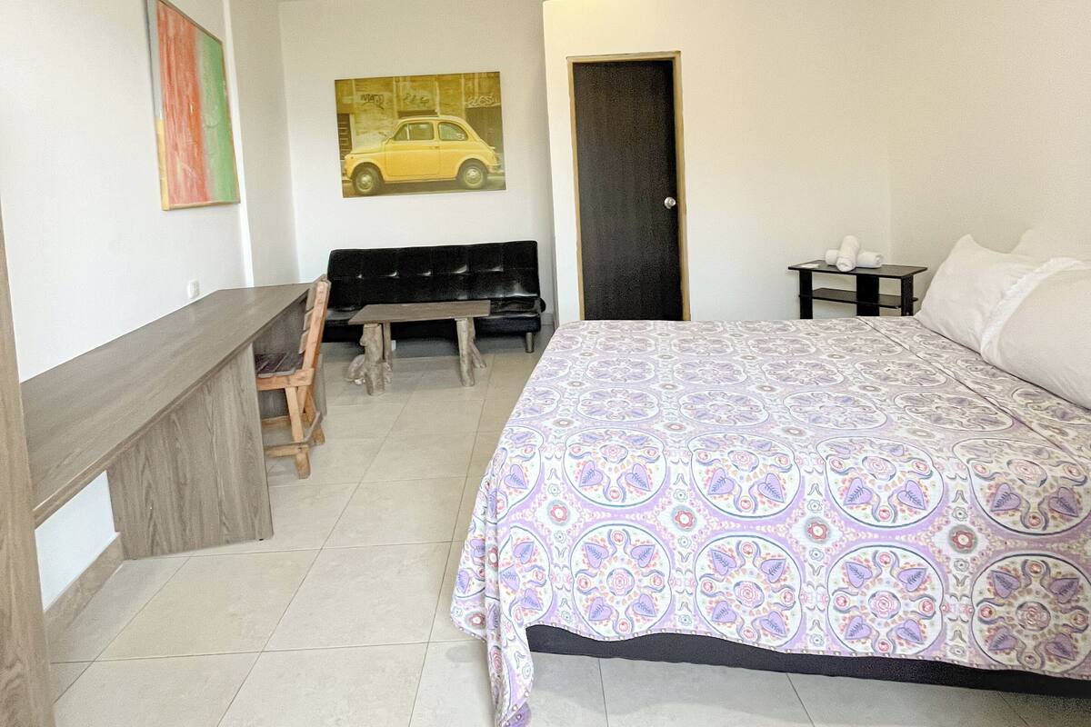 A bedroom with a bed, a desk, a chair, a bench, and a door.