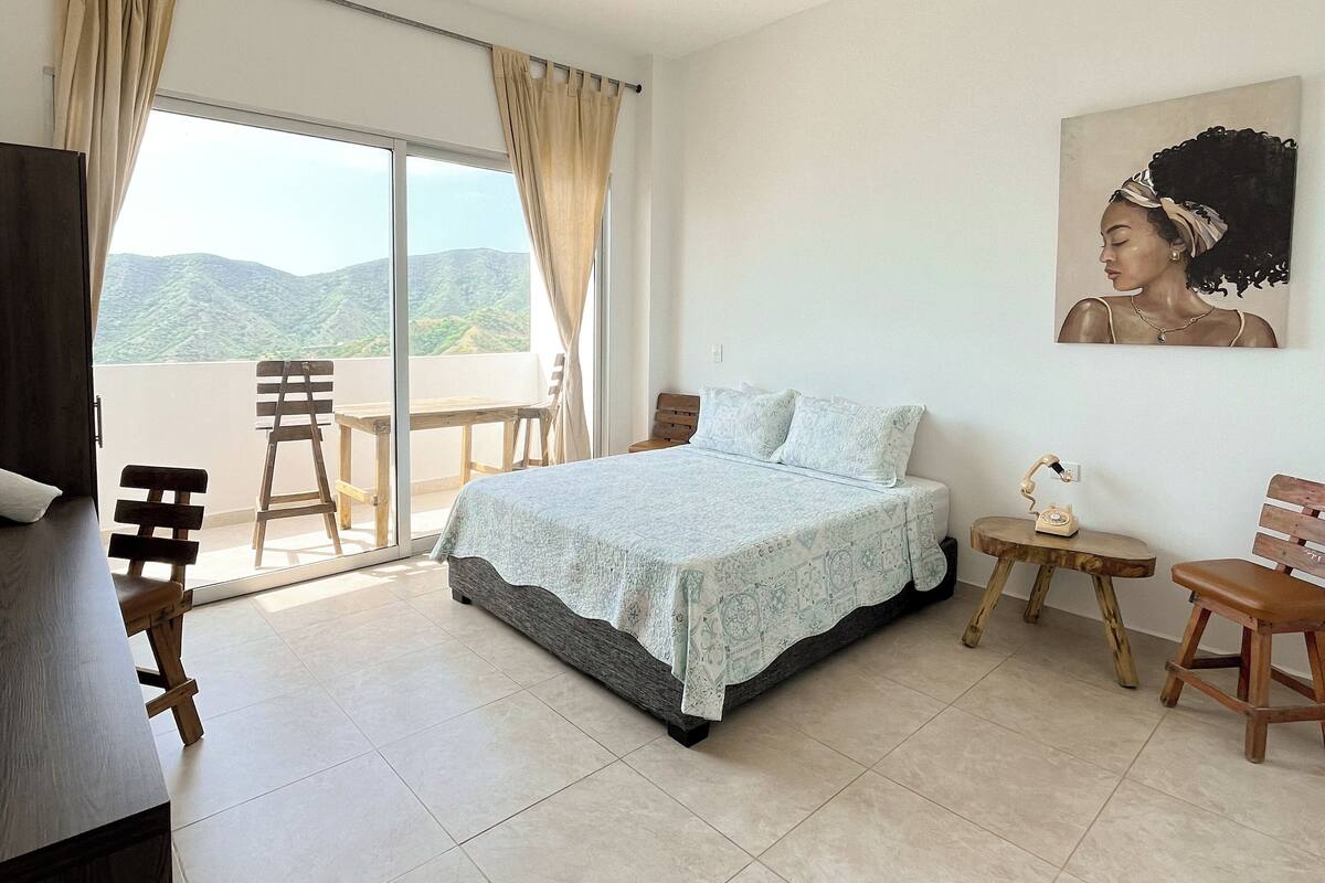 A bedroom with a bed, a desk, a chair, a table, and a painting on the wall.