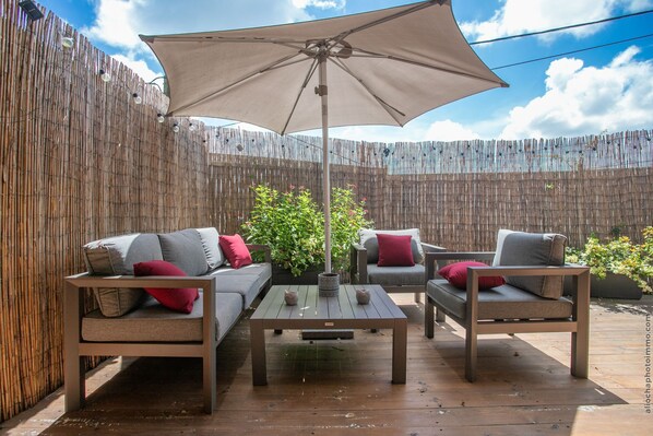 A patio with a wooden deck, two sofas, a coffee table, and an umbrella. - The cocooning area (Saint-Joseph)