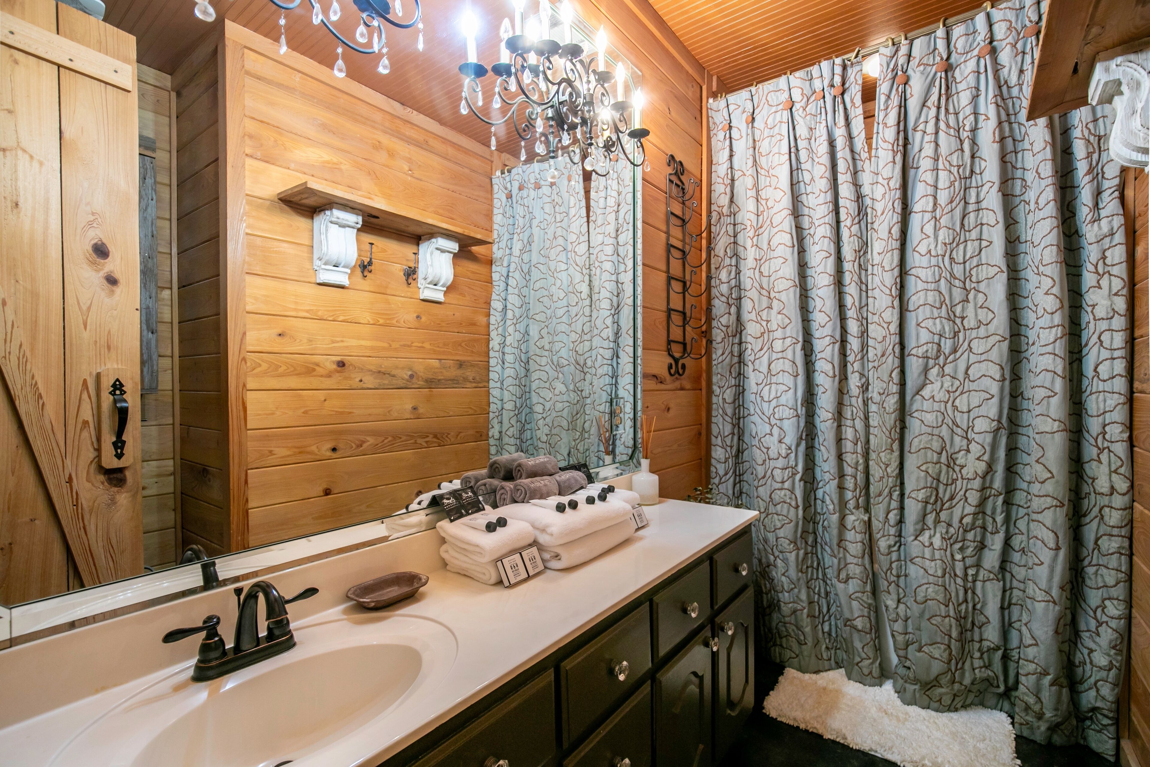 Ein Badezimmer im Holzblockhaus-Stil mit einem großen Spiegel, Holzschränken, einem Waschbecken und einer Pendelleuchte.